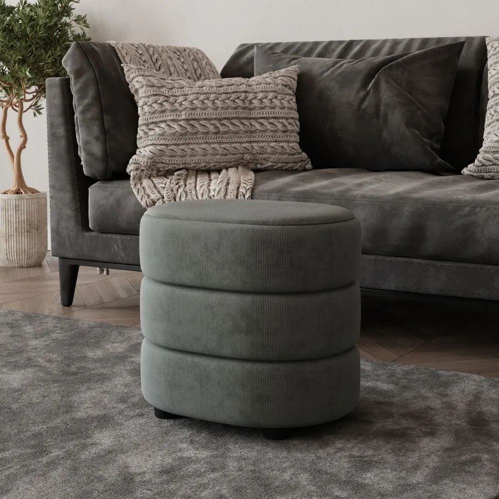 3D visualization of a round upholstered ottoman placed in front of a dark gray sofa with pillows